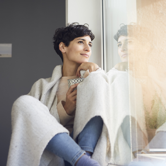 Frau sitzt auf der Fensterbank und schaut raus.
