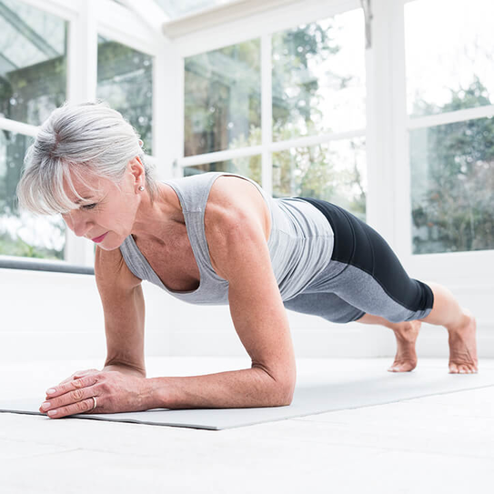 Ältere Frau macht Plank auf einer Yogamatte.