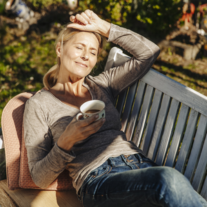 Frau liegt mit einer Tasse Tee in der Hand auf einer Gartenbank.